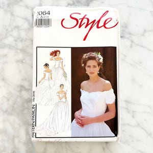 May include: A white sewing pattern package with the word "Style" in red script. The package features illustrations of wedding dresses and a photo of a woman in a white off-the-shoulder wedding dress. The pattern size is A (8-18).