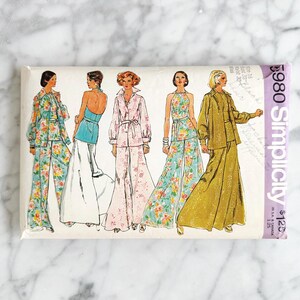 May include: Vintage Simplicity sewing pattern #980 for women's trousers and tops. The pattern features five different styles, including a floral print jumpsuit, a plain colour jumpsuit, a floral print top and trousers, a plain colour top and trousers, and a plain colour jacket and trousers. The pattern is printed on a white background with a purple border.