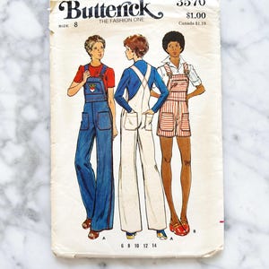 May include: Vintage sewing pattern for overalls, sizes 6-14. The pattern features three models wearing different styles of overalls: one in blue denim, one in white, and one in red and white striped fabric. The pattern is titled "Butterick The Fashion One" and has the number 3570.