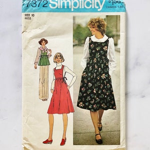 May include: Vintage Simplicity sewing pattern number 7372 for a dress with a bib and a skirt. The pattern is for size 10 miss. The pattern shows three different styles of the dress, one with a floral print, one with a red skirt, and one with a green skirt.