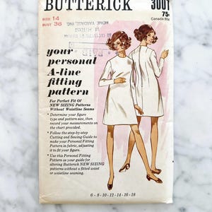 May include: Vintage Butterick sewing pattern envelope, size 14, bust 91 cm. Features an A-line dress design. Includes instructions for personal fitting. The envelope has text and illustrations.