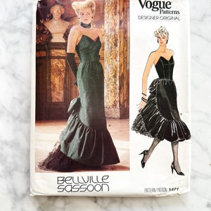 May include: A vintage Vogue Patterns sewing pattern featuring a green strapless evening gown with a ruffled hem and a black lace train. The pattern is labeled "Bellville Sassoon" and includes a design illustration. The text "Designer Original" is also visible.
