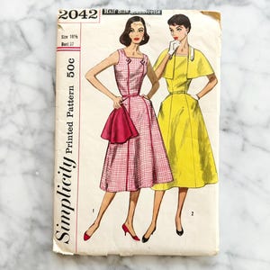 May include: Vintage Simplicity sewing pattern, number 2042, featuring illustrations of two dresses. One dress is pink and white checkered, the other is yellow. The pattern is for a half-size blendorette, size 16 1/2, bust 37.