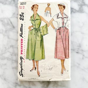 May include: Vintage Simplicity printed sewing pattern, featuring two dress designs. The pattern is marked with the number 3257, size 14, and bust 32. The price is 25 cents. The designs include a green dress and a red and white checkered dress.