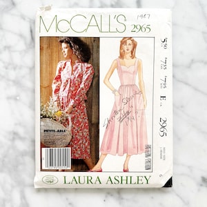 May include: Vintage McCall's sewing pattern for a dress and jacket by Laura Ashley. The pattern is for sizes 6-16 and includes instructions for a skirt with a gathered front and a fitted jacket with a V-neckline. The pattern is from 1987 and is in excellent condition.
