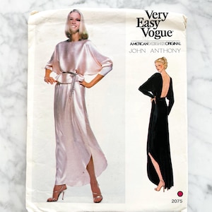 May include: A vintage Very Easy Vogue sewing pattern featuring a design by John Anthony. The pattern shows a long, flowing dress with a high slit and a cape-like top in a light pink color. The back of the dress is black with a low back and a high slit.