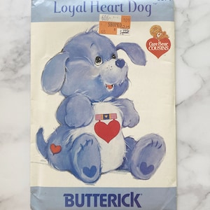May include: A vintage sewing pattern for a blue Care Bear Cousin dog plush toy. The pattern is titled "Loyal Heart Dog" and includes a picture of the finished plush toy. The pattern is from Butterick and has the number 3371.