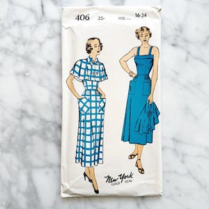 May include: Vintage sewing pattern featuring illustrations of two dresses. One dress is a blue and white checkered design, and the other is a solid blue dress. The pattern is labeled "406" and "New York Gold Seal", with size information.