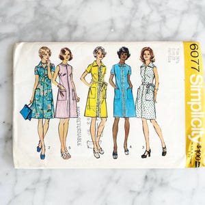 May include: A vintage Simplicity sewing pattern with illustrations of five dresses in different styles and colours. The dresses include floral, striped, and polka dot patterns. The pattern is labelled "6077 Simplicity".