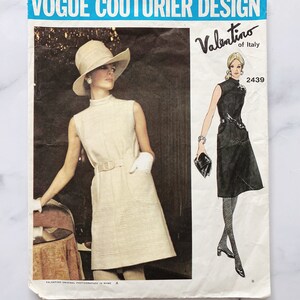 Puede incluir: Patrón de diseño de alta costura Vogue para un vestido de Valentino de Italia. El número del patrón es 2439. La imagen muestra dos modelos que llevan el vestido en diferentes colores. Una modelo lleva un vestido blanco con un sombrero y la otra lleva un vestido negro con medias negras y tacones.