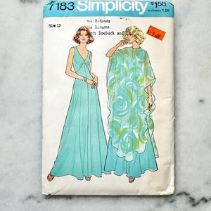 May include: Vintage Simplicity sewing pattern number 7183 for a maxi dress with a V-neck and a cape. The pattern is for size 12 and includes instructions for making the dress in a blue and green floral print.