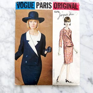May include: Vintage Vogue Paris Original sewing pattern number 1376 by Jacques Heim. The pattern features a black and white double-breasted suit with a skirt and a matching jacket. The model is wearing a black hat and gloves.
