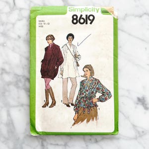 Könnte beinhalten: Vintage Simplicity Schnittmuster Nummer 8619 für die Größen 10-12. Das Schnittmuster umfasst drei verschiedene Stile: eine langärmelige Bluse mit einer Schleife in der Taille, eine langärmelige Tunika mit Kragen und eine langärmelige Jacke mit Kragen.