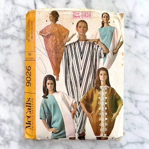 May include: A vintage McCall's 9026 sewing pattern envelope featuring illustrations of four different dress styles. The cover displays the text Time Saver QUICKIE, McCall's, and 9026, showcasing garments in orange swirl, black and white stripes, teal and white, and brown with white floral trim.