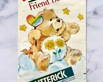 May include: Vintage Butterick sewing pattern featuring Friend Bear from Care Bears. The illustration shows a tan bear holding a flower-adorned ball, with a rainbow heart and yellow stars. The pattern is on a cream-colored background.
