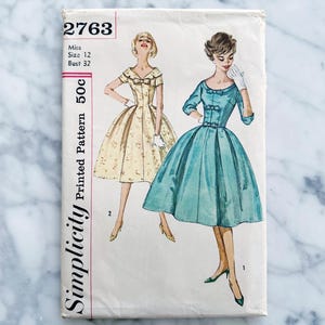 May include: Vintage Simplicity sewing pattern number 2763 for a dress. The pattern is for a miss, size 12, bust 32. The pattern shows two different styles of dresses, one with a floral print and one in a solid blue color. The pattern is printed on white paper with black text.