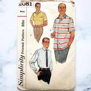 May include: Vintage Simplicity printed pattern 2081 for men's shirts. The pattern features illustrations of three shirt designs: a yellow floral short-sleeve shirt, a striped short-sleeve shirt, and a striped long-sleeve shirt with a tie. The pattern is marked "Medium".