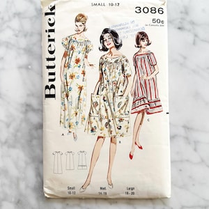 Puede incluir: Sobre de patrón de costura Butterick vintage con ilustraciones de tres vestidos. El sobre está etiquetado como "Small 10-12" e incluye el número "3086". Los vestidos se muestran con estampados florales, a rayas y lisos.