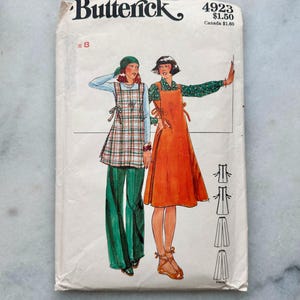 May include: A Butterick 4923 sewing pattern envelope featuring illustrations of two outfits: a plaid tunic with green trousers and a solid orange sleeveless dress. The envelope includes the pattern number 4923 and size 8 printed on the front.