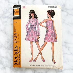 May include: Vintage McCall's sewing pattern 9734 for a robe and nightgown. The pattern is for misses' sizes 12-34 and includes a step-by-step guide. The pattern features a floral print and is designed by Ajli of Slumbertogs.