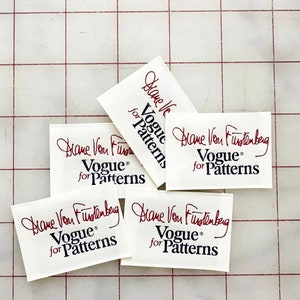 K&ouml;nnte beinhalten: Vier wei&szlig;e Stoff-Etiketten mit roter Schrift, die "Diane Von Furstenberg" lautet, und schwarzem Text, der "Vogue&reg; for Patterns" lautet.