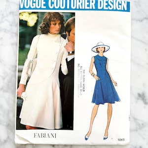 May include: Vintage Vogue Couturier Design sewing pattern for a dress. The pattern is for a white dress with a button-up front and a blue dress with a sleeveless bodice. The pattern number is 1065.