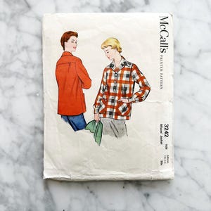 May include: Vintage McCall's Misses' Jacket sewing pattern. The pattern cover features illustrations of two women wearing jackets. One jacket is solid orange, and the other is a red, black, and white plaid. The pattern number is 3242, and the size is small.