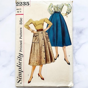 May include: Vintage Simplicity sewing pattern number 2235 for a skirt. The pattern is for a size 25 waist and 34 hip. The pattern shows two women wearing different skirts. One skirt is a blue, full-circle skirt. The other skirt is a brown and white patterned skirt with a button-up front and pockets.