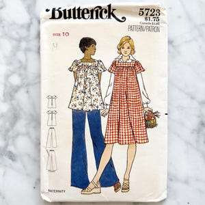 Puede incluir: Patrón de costura vintage para un vestido y pantalones de maternidad. El patrón es de Butterick y es talla 10. El patrón es para un vestido con estampado de cuadros vichy y un pantalón con estampado floral.