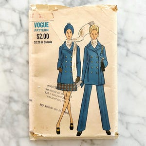 Puede incluir: Sobre de patrón Vogue vintage con ilustraciones de mujeres con abrigos y trajes de pantalón azules. El sobre tiene el texto "VOGUE PATTERN". El sobre está ligeramente desgastado con arrugas y decoloración visibles.