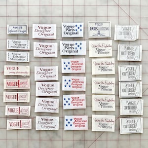 K&ouml;nnte beinhalten: Eine Sammlung von Vintage-Stoffetiketten in Wei&szlig; mit roter, blauer und schwarzer Schrift. Die Etiketten tragen die W&ouml;rter "Vogue", "Designer", "Original", "Paris", "Couturier", "Special Design", "young fashionables", "American" und "Diane Von Furstenberg".