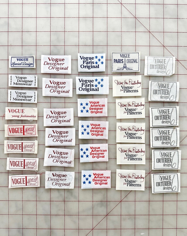 K&ouml;nnte beinhalten: Eine Sammlung von Vintage-Stoffetiketten in Wei&szlig; mit roter, blauer und schwarzer Schrift. Die Etiketten tragen die W&ouml;rter "Vogue", "Designer", "Original", "Paris", "Couturier", "Special Design", "young fashionables", "American" und "Diane Von Furstenberg".