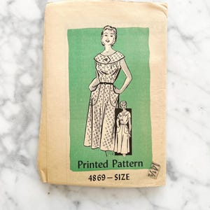 May include: Vintage sewing pattern for a dress with a green background. The pattern number is 4869. The pattern is for a sleeveless dress with a round neckline and a gathered skirt.