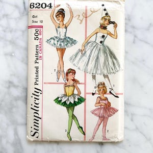 May include: Vintage Simplicity sewing pattern number 6204 for a girl's ballet costume. The pattern includes three different costume designs: a white tutu with a clown hat, a green tutu with a flower design, and a pink tutu. The pattern is for size 10 and costs 50 cents.