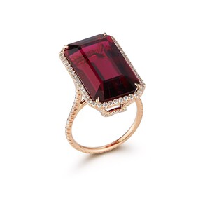 May include: A rose gold ring with a large, rectangular, dark red gemstone surrounded by a halo of smaller, white gemstones.