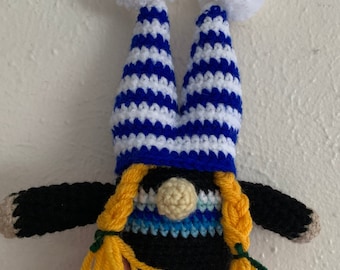 May include: A crocheted gnome with a blue and white striped hat, yellow hair, and a blue, green, and white striped scarf.