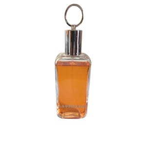 May include: A clear, rectangular perfume bottle with an orange liquid inside. The bottle has a silver cap and a small, round silver handle. The brand name "LAGERFELD" is printed on the front of the bottle.