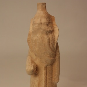 May include: A wooden sculpture of a person in a long robe. The sculpture is carved with intricate details and has a rustic, handmade look.