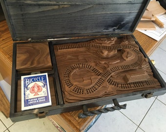 May include: A wooden game board with a carved track, a deck of Bicycle playing cards, and a wooden box with a rope handle.