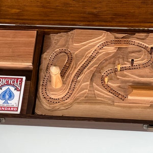 May include: A wooden box with a carved wooden game board inside. The game board features a winding track and a small wooden tower. A deck of Bicycle playing cards is also included in the box.