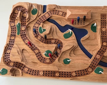 May include: A wooden game board with a golf course design. The board features a blue lake, green golf courses, and white golf flags. The board is made of wood and has a natural finish. The board is numbered from 1 to 115. There are red and blue pegs on the board.