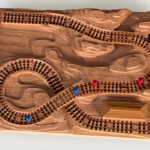 May include: A wooden game board with a winding track, numbered spaces, and a wooden bridge. There are blue, red, and black playing pieces on the board.