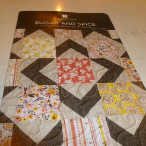 May include: A full-size quilt pattern titled "Sugar and Spice" featuring a patchwork design. The quilt incorporates various floral and geometric patterns in shades of brown, yellow, peach, and white. The quilt measures 82.5" x 91.5".