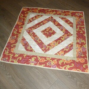 May include: A red, white, and beige quilted throw pillow with a floral pattern. The pillow has a square shape and a geometric design in the center.