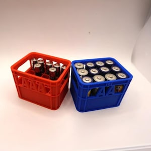 Pode incluir: Duas caixas de plástico, uma vermelha e outra azul, cheias de pilhas. A caixa vermelha contém pilhas cilíndricas, enquanto a caixa azul está cheia de pilhas AA. As caixas estão sobre uma superfície branca.