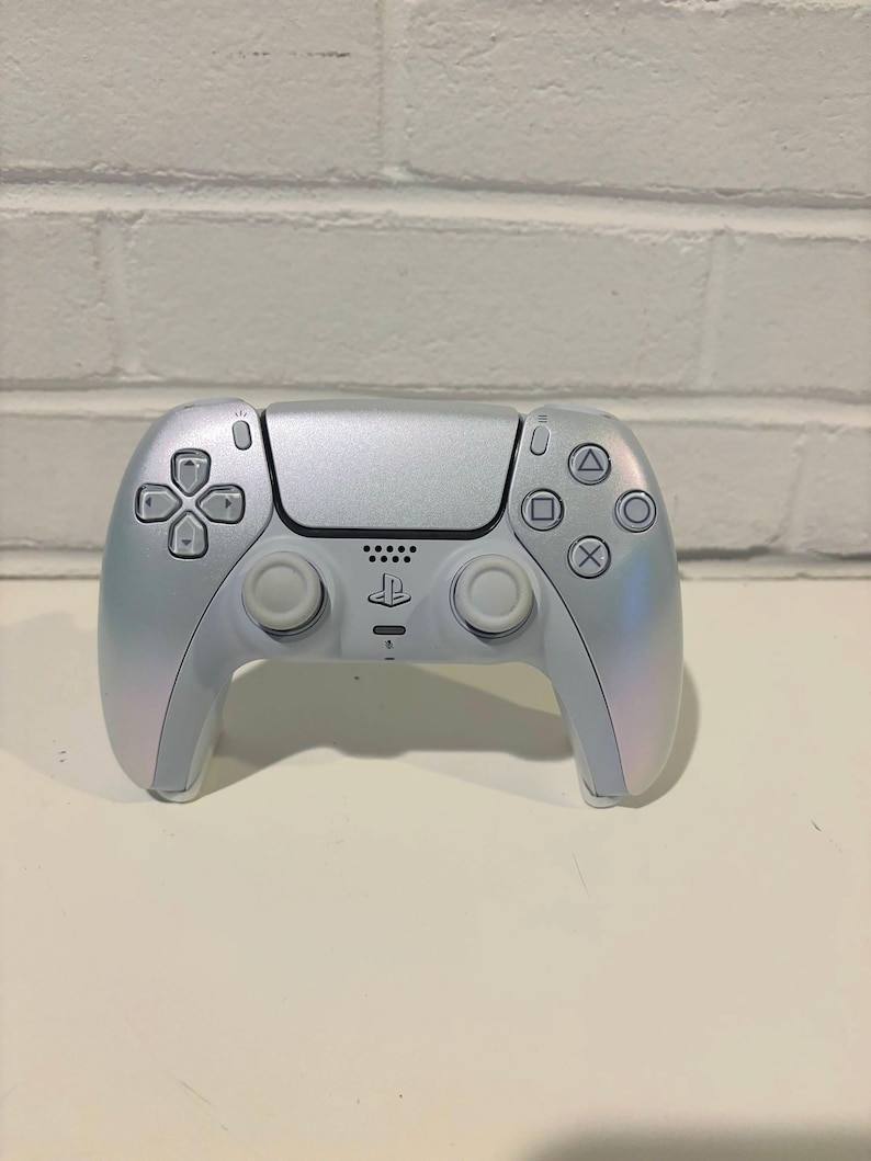Pu&ograve; includere: Un controller wireless DualSense bianco per PlayStation 5 con finitura perlata. Il controller ha un logo PlayStation nero e un touchpad nero.