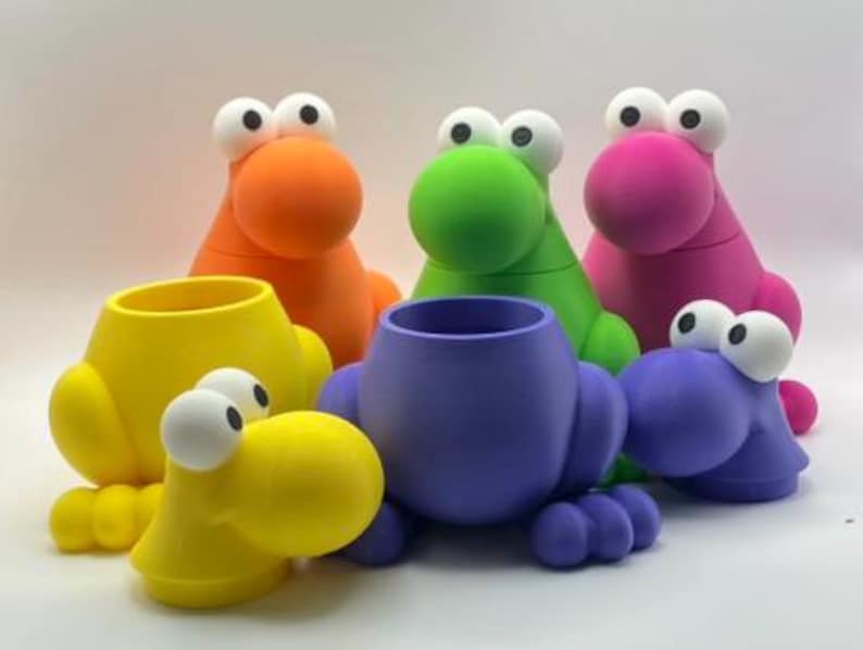 May include: A collection of six whimsical, colorful creature-shaped containers. The containers are in shades of yellow, orange, green, pink, purple, and blue. Each has large, white-eyed, round faces and a cylindrical opening.