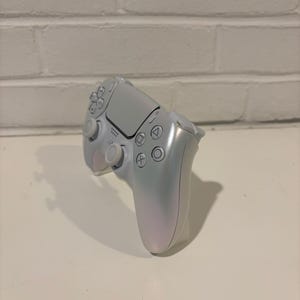 Pu&ograve; includere: Un controller PlayStation 5 DualSense bianco con una finitura perlata. Il controller ha una piastra frontale bianca con il logo PlayStation e pulsanti.