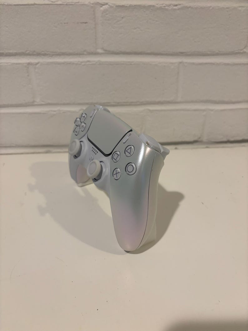 Pu&ograve; includere: Un controller PlayStation 5 DualSense bianco con una finitura perlata. Il controller ha una piastra frontale bianca con il logo PlayStation e pulsanti.