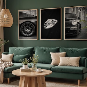 May include: Three black and white framed prints of a Porsche car. The prints are hanging on a green wall above a green sofa with beige cushions.